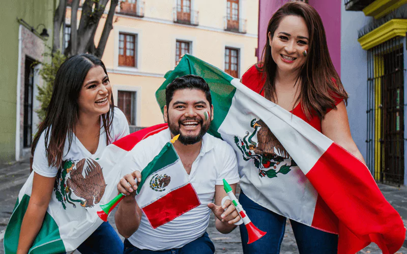 A man and two women celebrating with Mexican flags on the street