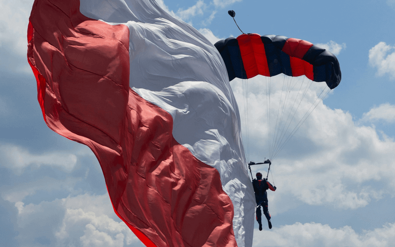 A man gliding parachute with a large white and red Polish flag