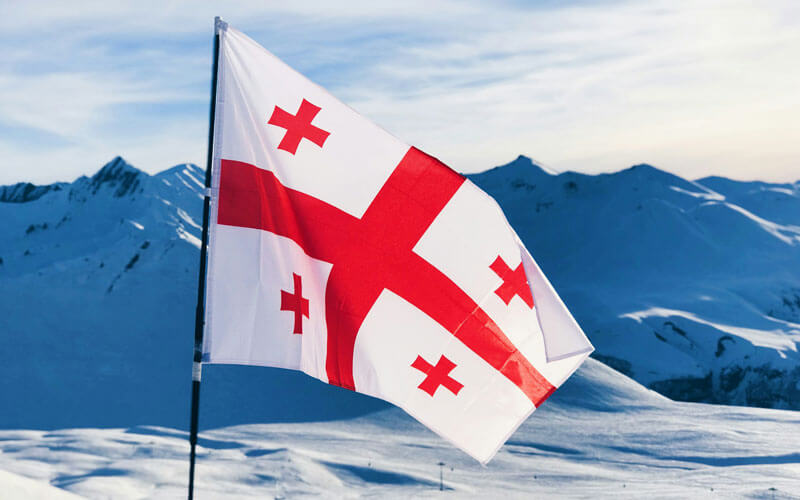 Red and white flag of Georgia at the snow capped mountain