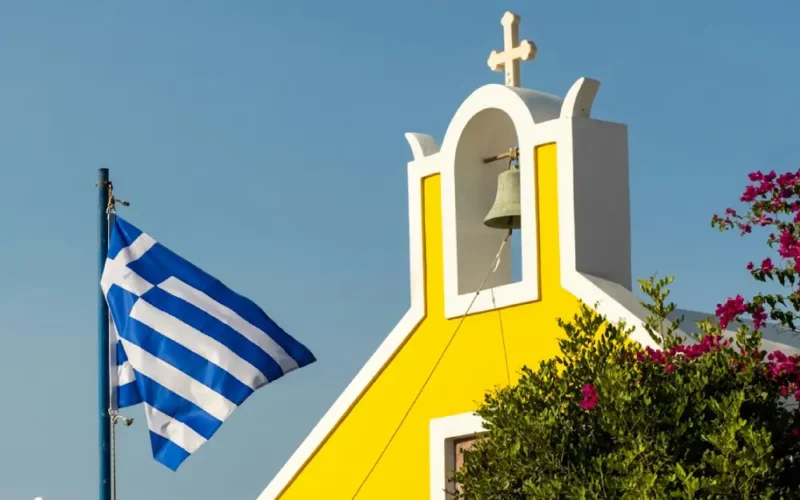 Blue and white Greek flag infront of the yellow painted Church