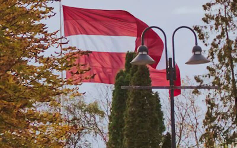 Flag of Latvia behind the woods and lamp-post flying in the sky