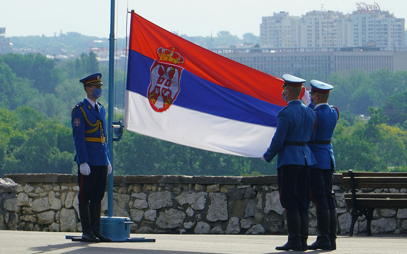 Men in uniform holding red, blue and white Serbian flag