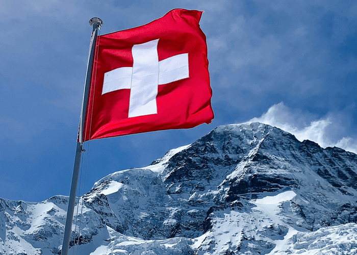 Red and white Swiss flag flying over the snowy mountain peak