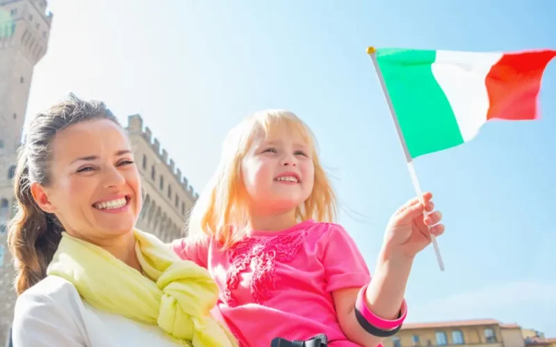Woman carrying girl holding a small Italian flag